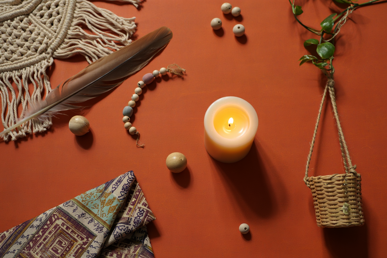 Décoration bohème chic: ambiance chaleureuse avec candle, plumes, perles et sac en osier sur fond orange, textiles à motifs, esprit bohème élégant.